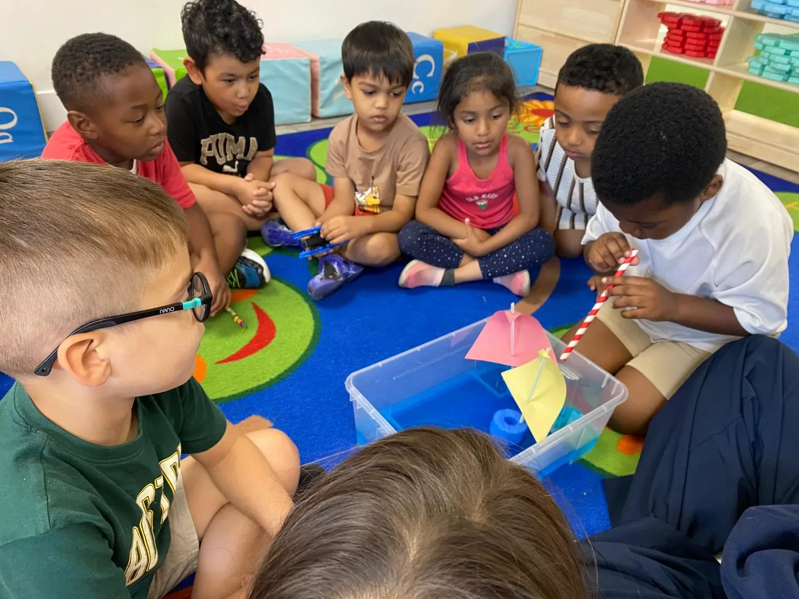 Children gathered around a water tray experimenting with paper sailboats