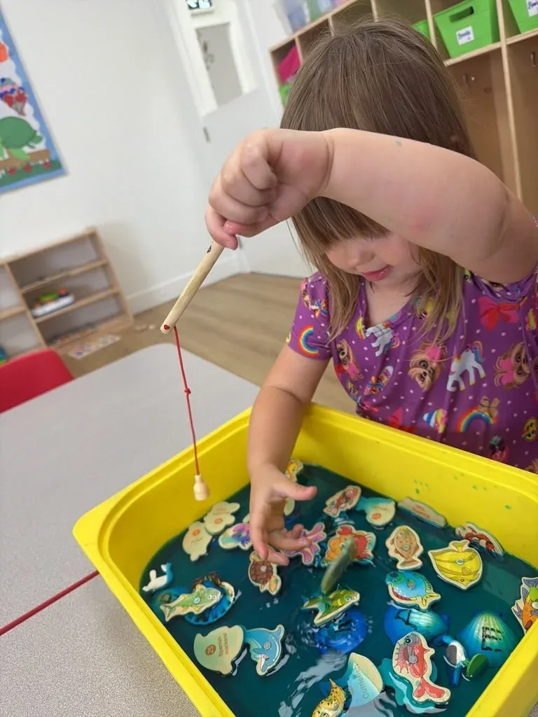 A child using a magnetic fishing rod to catch wooden fish in a water tray