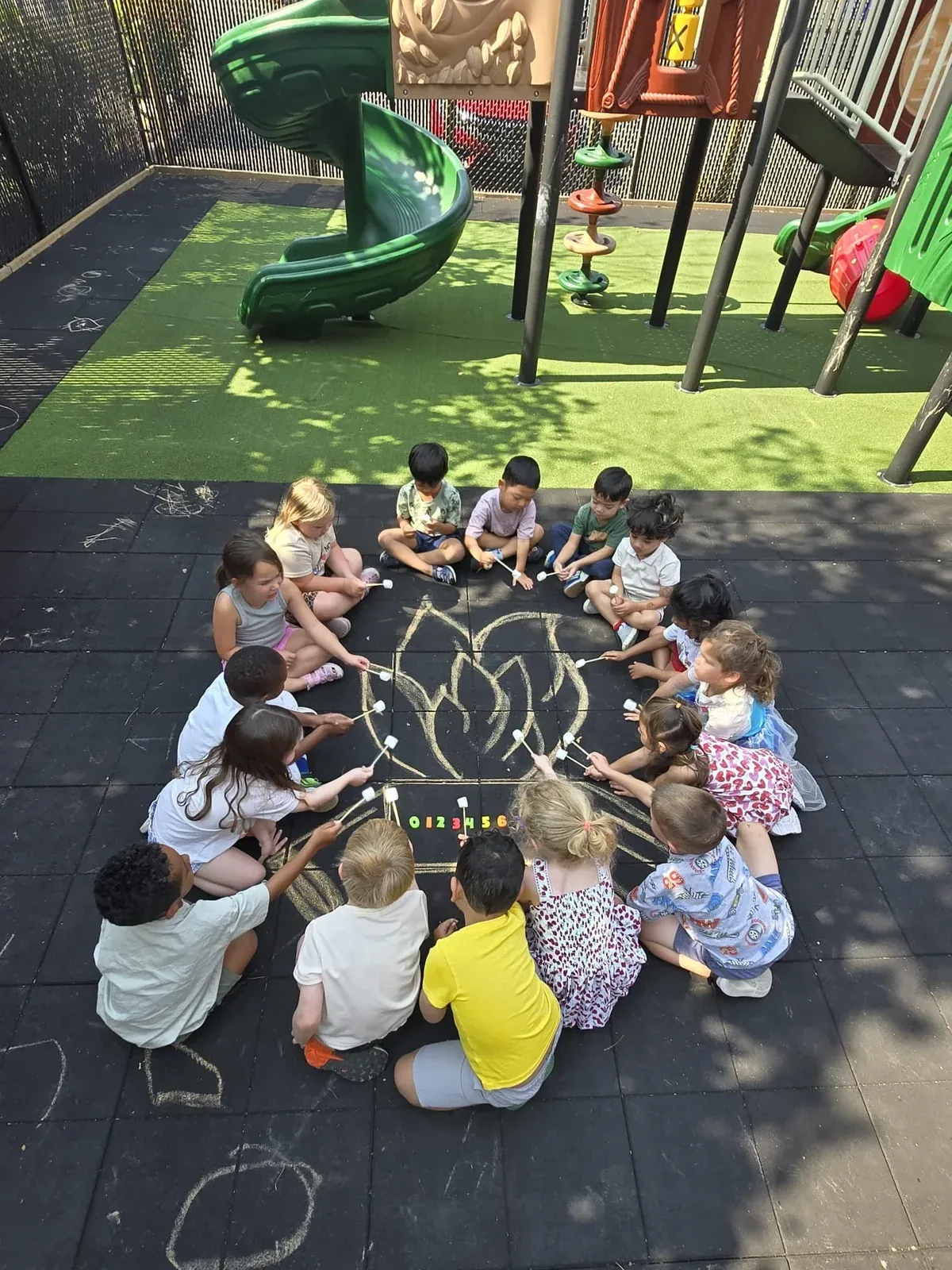 Children sitting in a circle around a chalk campfire drawing on the playground