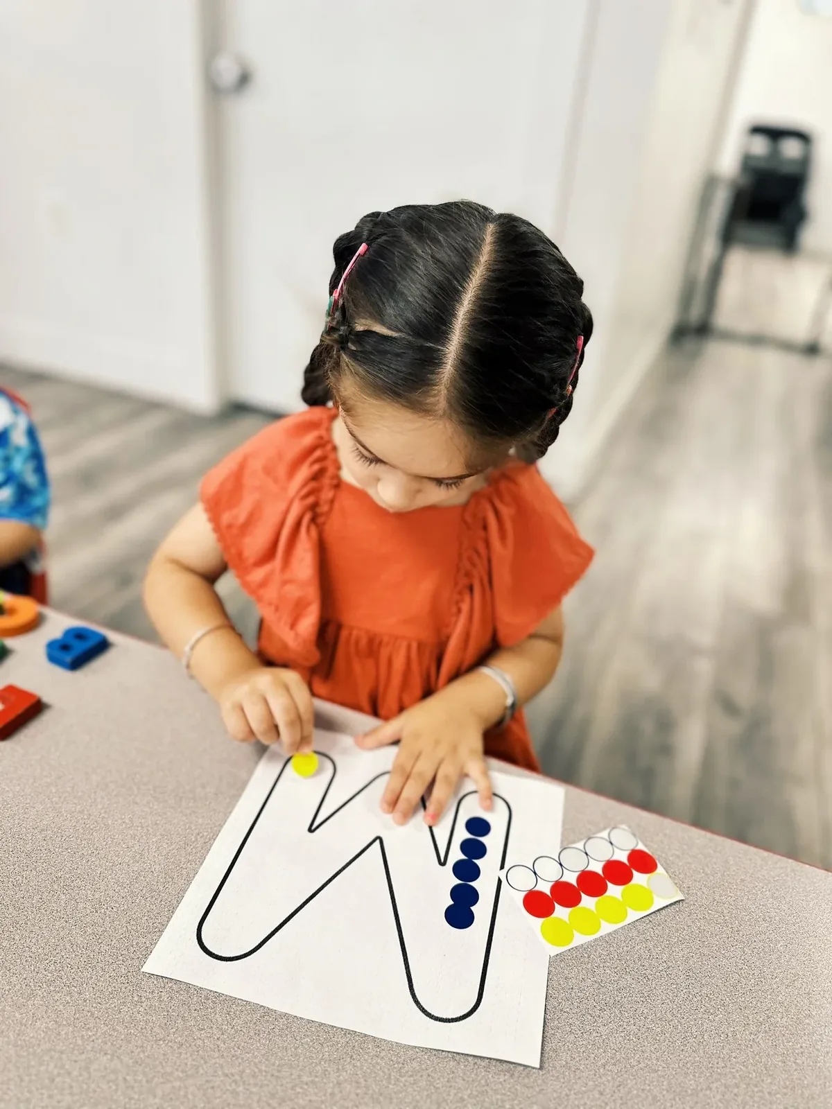 A child placing coloured dot stickers along the outline of the letter W