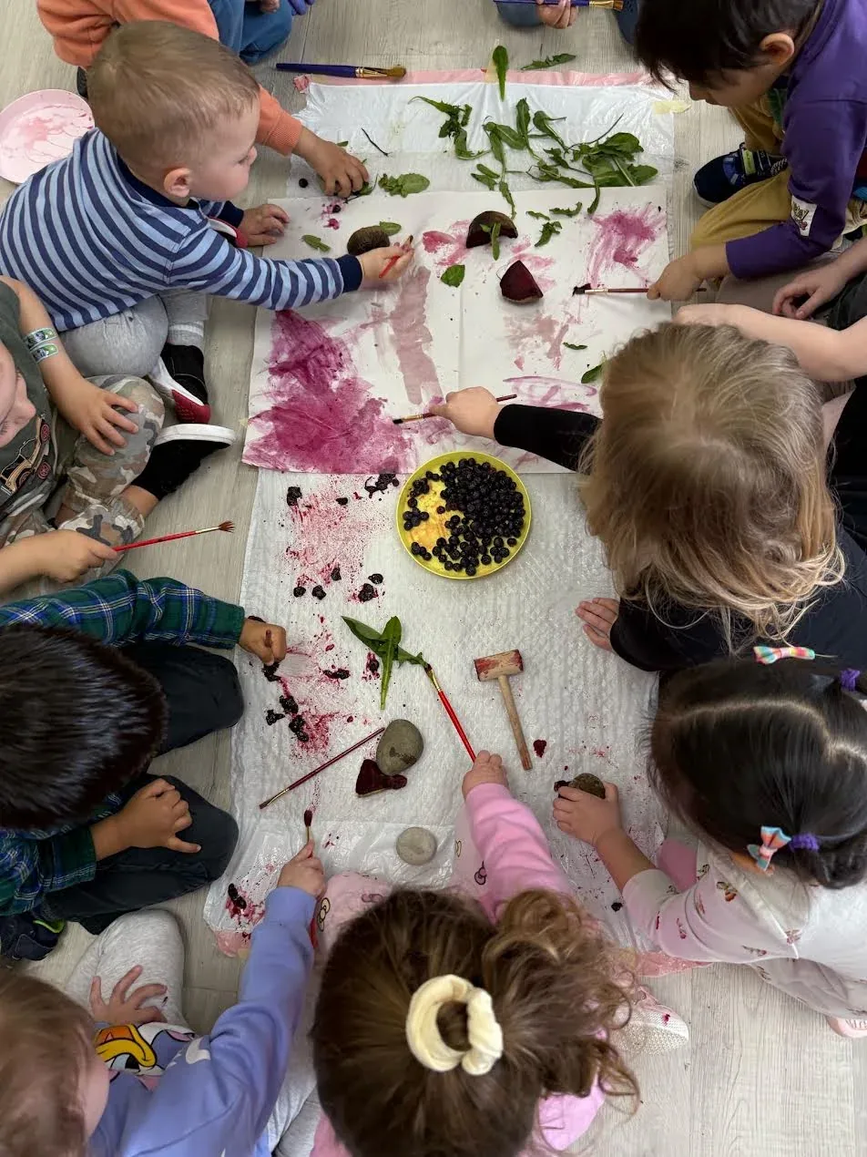 A large group of children painting together with berries and natural materials on the floor