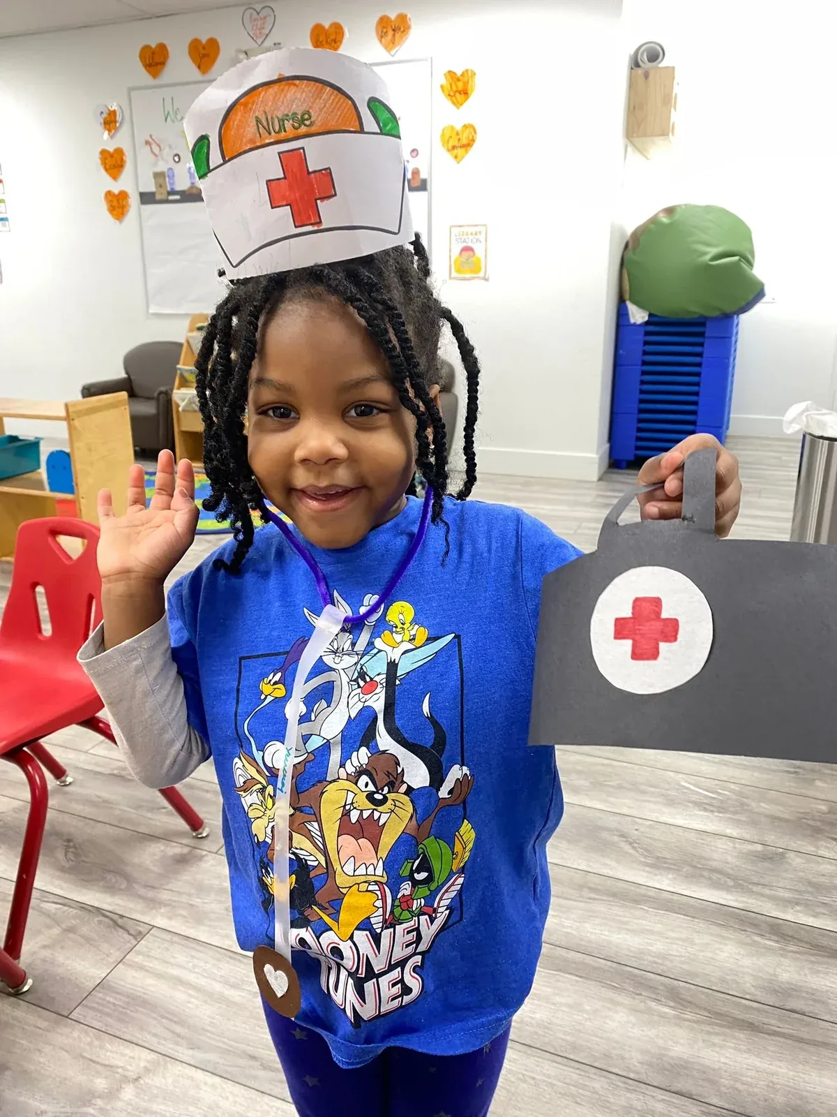 A smiling child dressed up as a nurse with a handmade cap and medical kit
