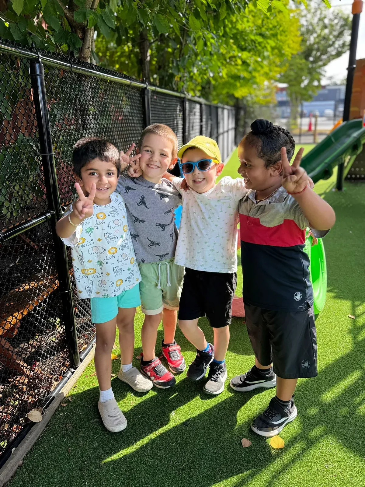 Four children with arms around each other making peace signs on the playground