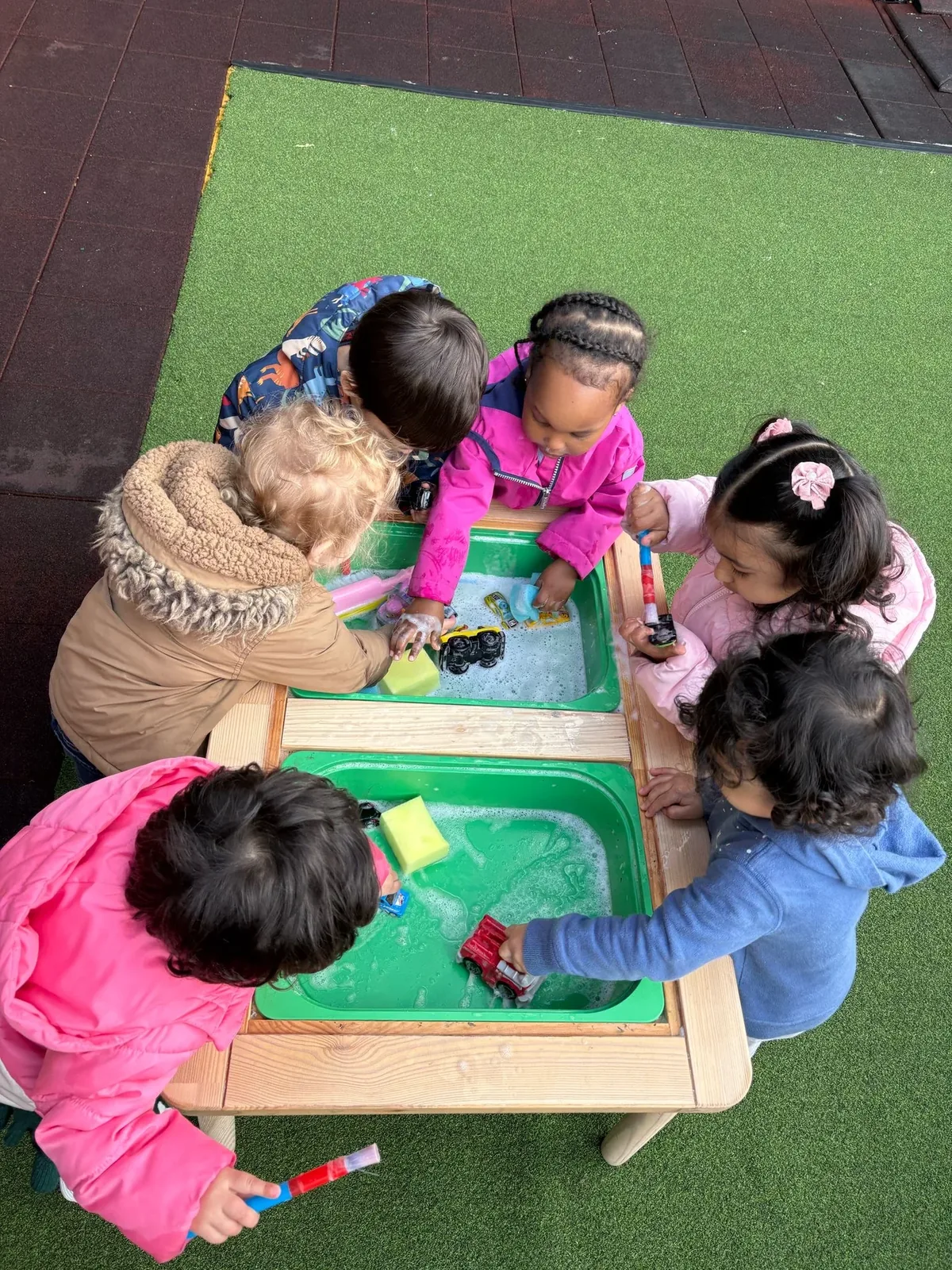 A group of children washing toy cars together at an outdoor water table