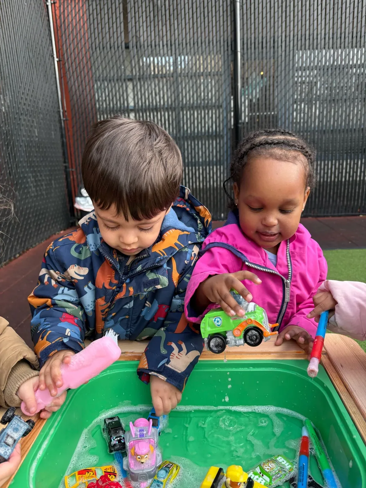 Two children playing together at an outdoor water table with toy cars